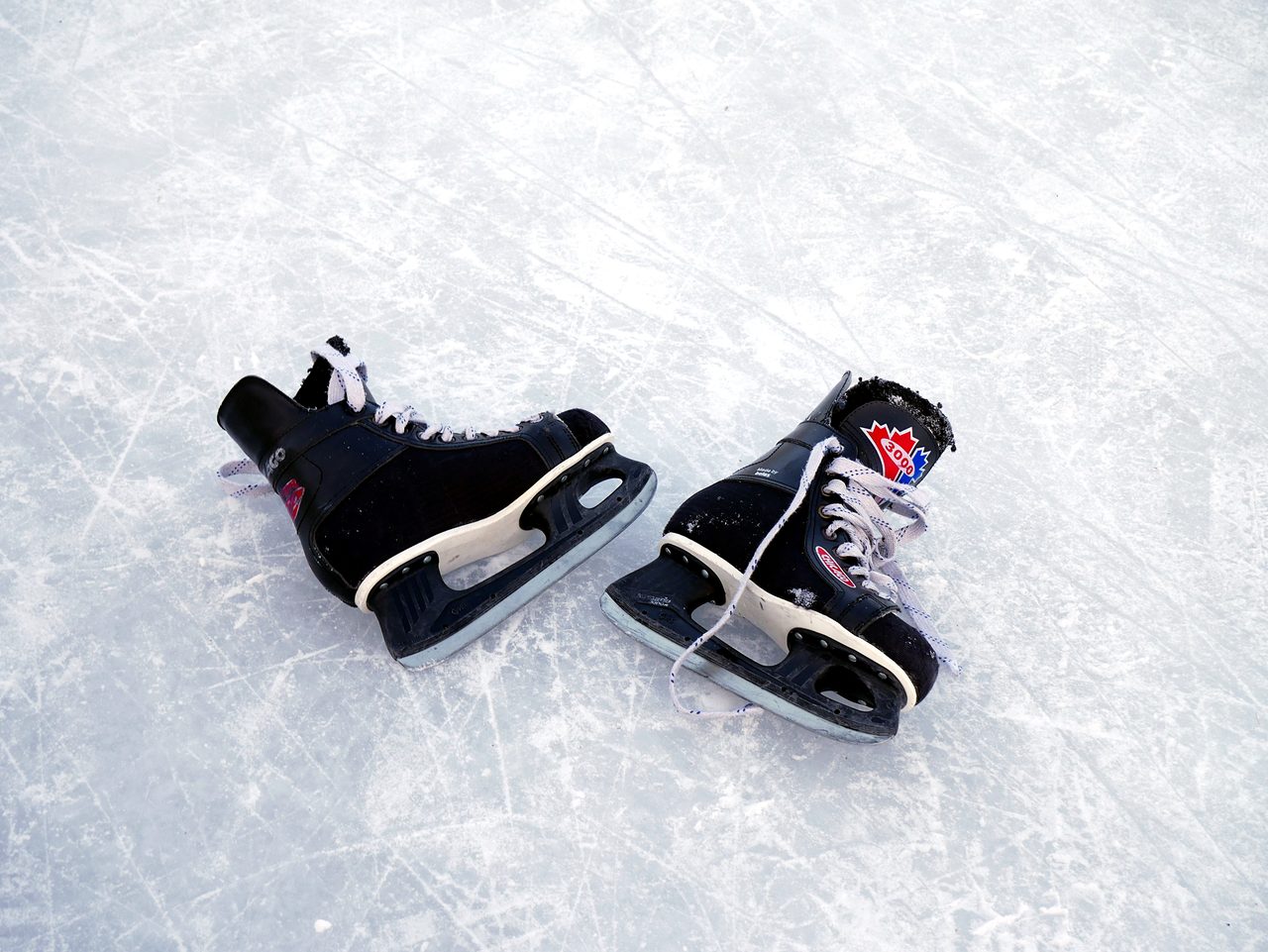 A pair of black hockey skates lying on outdoor ice